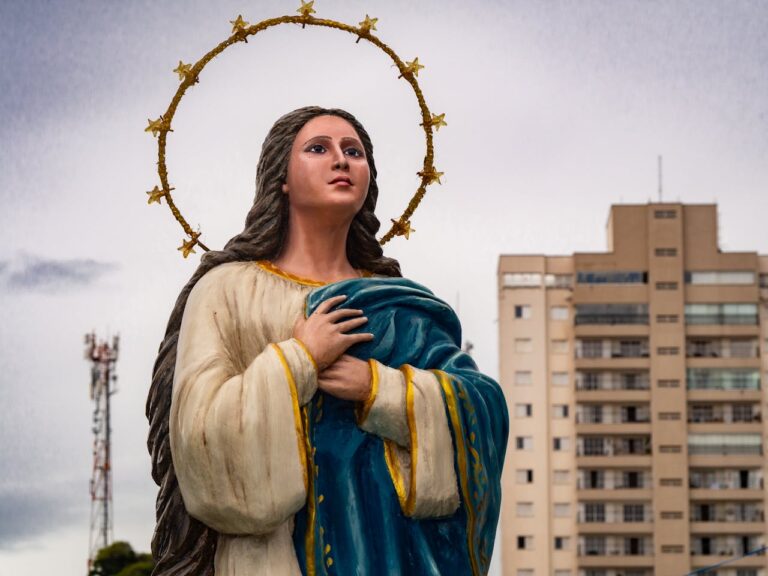 A beautiful statue of the Virgin Mary with a halo, set against a city backdrop, symbolizes peace and faith.