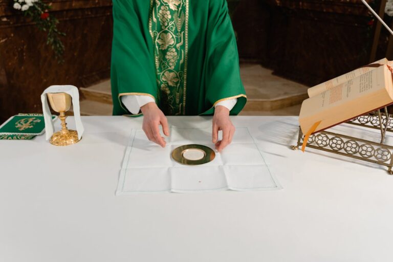 A priest in green vestments prepares the sacramental bread during a Catholic mass ceremony.